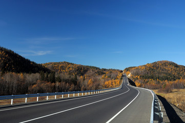 Highway in the Valley. Bright autumn landscape. The blue sky and mountains on the horizon. Used toning of the photo.