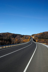 Highway in the Valley. Bright autumn landscape. The blue sky and mountains on the horizon. Used toning of the photo.