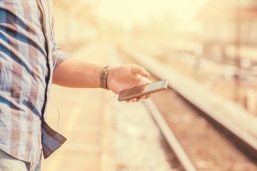 Male tourists are carrying a smartphone headphone jack. Standing near the train tracks, warm tone.