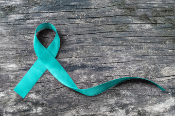 Teal ribbon awareness to support Ovarian Cancer PCOS on human hand with old aged wood background: Satin silk symbolic concept for raising concerns/ help and campaign on people living with illness