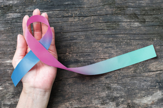 Thyroid Cancer Awareness ribbon Teal Pink Blue color ribbon on woman helping hand w/ old aged wood background: Satin fabric loop symbolic logo raising support help people life living w/ tumor illness