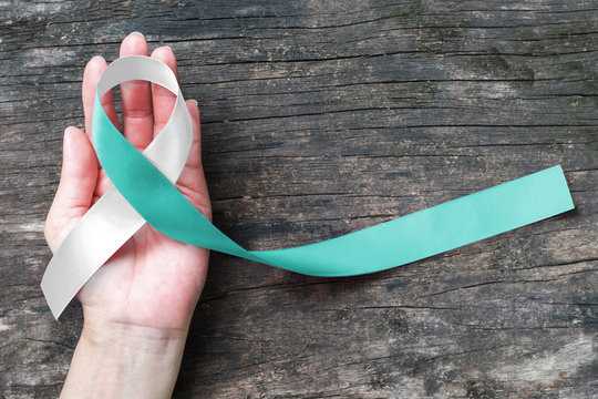 Teal White ribbon awareness support Cervical Cancer on human hand with old aged wood  background: Satin silk ribbon symbolic concept for raising concerns/ help/ campaign on people living with illness