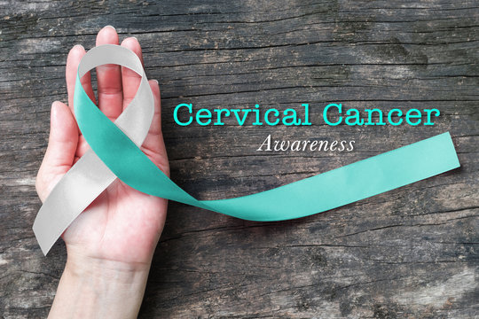 Teal White ribbon awareness support Cervical Cancer on human hand with old aged wood  background: Satin silk ribbon symbolic concept for raising concerns/ help/ campaign on people living with illness