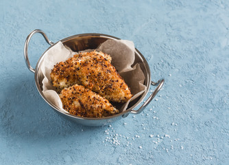Quinoa crusted chicken in a metal bowl. On a blue background.