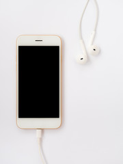Close-up image of new smartphone connect with charging cable (Lightning) and earbuds on white background with copy space.
