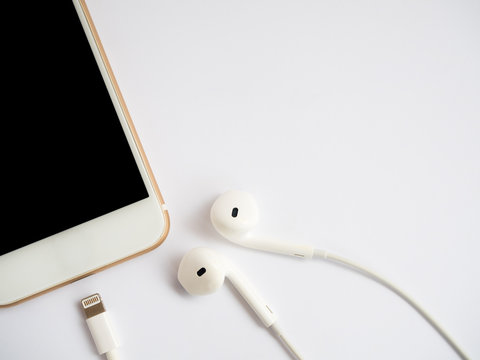 Close-up image of new smartphone, earbuds and charging cable (Lightning) on white background with copy space.
