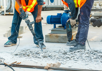 Builder worker with pneumatic hammer drill equipment breaking concrete at road construction site