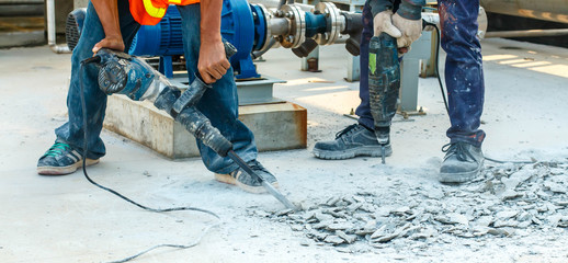 Builder worker with pneumatic hammer drill equipment breaking concrete at road construction site