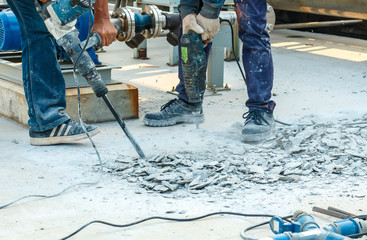 Builder worker with pneumatic hammer drill equipment breaking concrete at road construction site