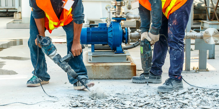 Builder worker with pneumatic hammer drill equipment breaking concrete at road construction site