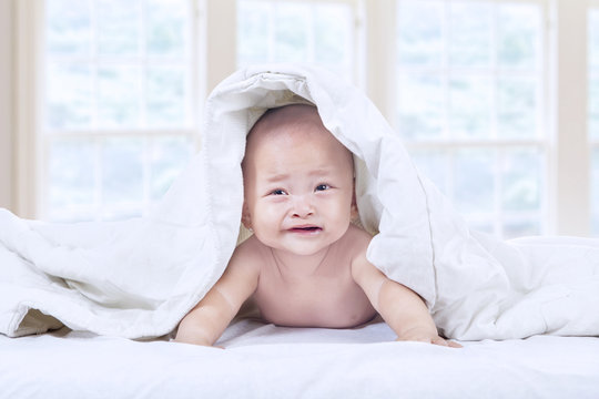 Cute baby crying under blanket at home
