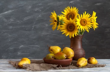 Poster Still life: a set of pottery, a bouquet of sunflowers and pears on a wooden table. Natural light from the windows. © symbol344