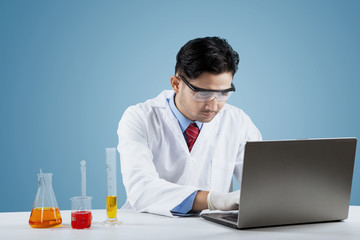 Scientist with chemical liquid and laptop