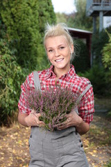 Hübsche blonde Frau im Garten beim Umtopfen von Heidekraut im Herbst
