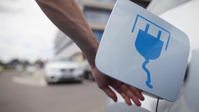 Color footage of a man's hand closing the lid of an electrical car, after charging.