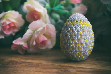Easter egg from beads next to pink roses