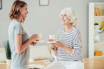 Cheerful woman and her adult daughter drinking tea