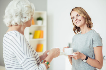 Positive woman drinking coffee with her aged mother