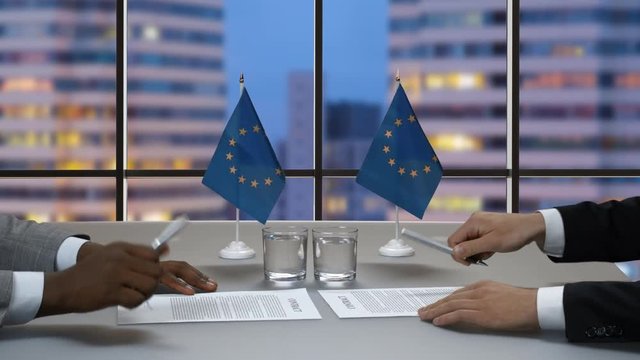 Male hands signing papers. Businessmen's handshake near EU flags. Build a strong alliance. Step towards success.