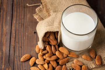 Almond milk in a glass with almond nuts on a wooden table. Healthy food and drink concept.