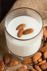 Almond milk in a glass with almond nuts on a wooden table. Healthy food and drink concept.