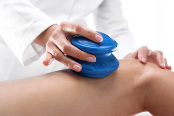 Masaż odchudzający, modelowanie sylwetki. Kosmetyczka masuje uda kobiety gumowymi bańkami do masażu.