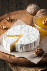 Brie type of cheese. Camembert cheese. Fresh Brie cheese and a slice on a wooden board with nuts, honey and leaves. Italian, French cheese.