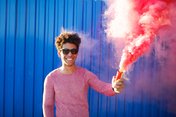 young black hipster man smiling and holding a colorful pink smoke