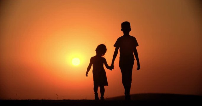 silhouette of two children, a brother and sister walking holding hands, slow motion