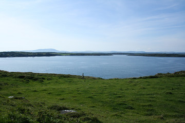 Woman in green fields staring into the distance near the sea