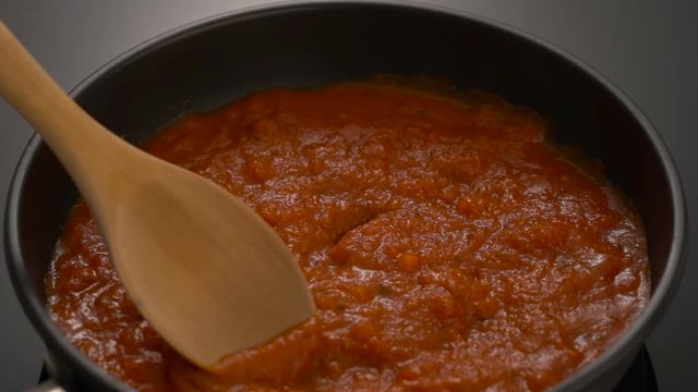 Bubbling hot tomato sauce for pasta, cooking in pan with wooden spatula.