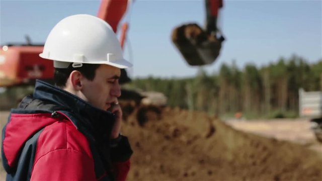 The builder in white helmet talking on a mobile phone.
