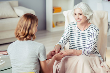 Positive aged woman holding hands of her granddaughter