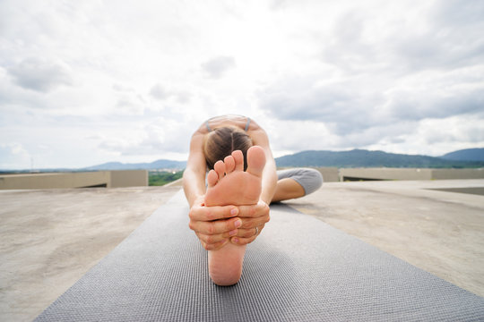 Yoga on rooftop. Young woman stretching on roof with city and mountains view.