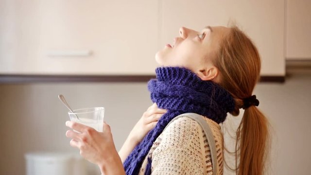 Girl with quinsy taking medicine and gargling throat in kitchen