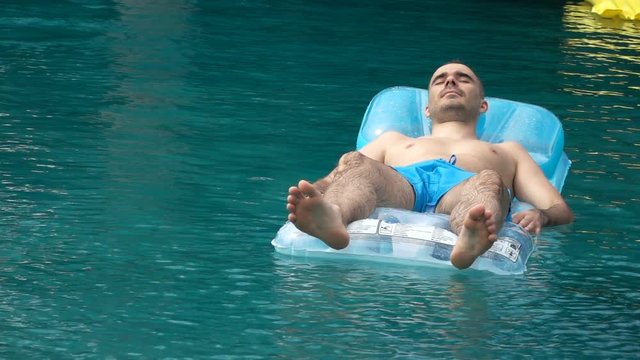 Young man lying on floating mattress in the pool, super slow motion

