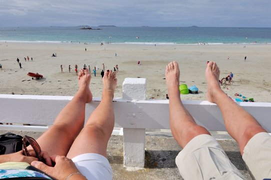 Un couple en vacances bien install&eacute; les jambes nues face &agrave; la plage en Bretagne
