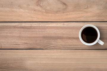 A cup of coffee is on top of wood table. Top view with copy spac