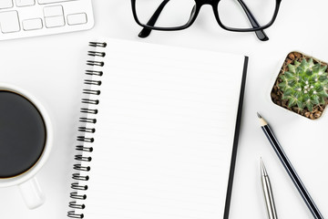 Empty notebook page is on top of white office desk table with supplies. Top view, flat lay.