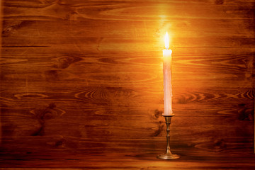 burning old candle with vintage brass candlestick on wooden back