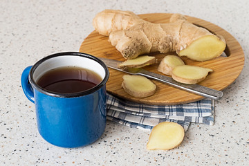 Tea and ginger root.    The enamel mug with hot tea, ginger root and knife on the cutting board, on the kitchen table.