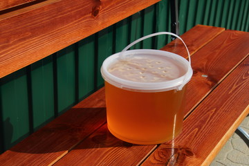 Plastic bucket with freshly collected wildflower honey on the garden bench