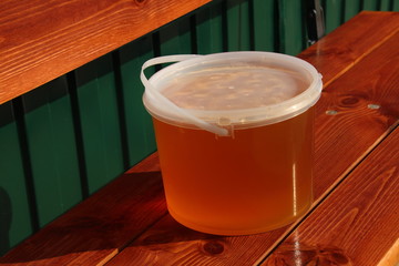 Plastic bucket with freshly collected wildflower honey on the garden bench © argot