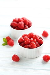 Red raspberries in bowl on a white wooden table