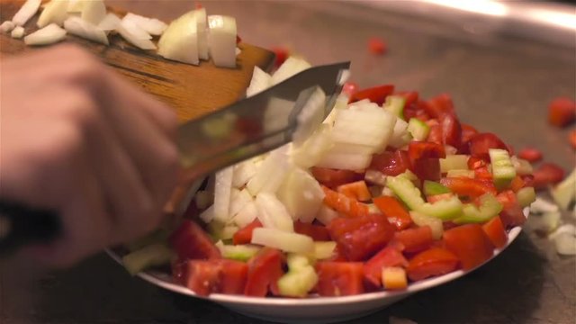 Chopped onion falls from utting Board to vegetables in dish