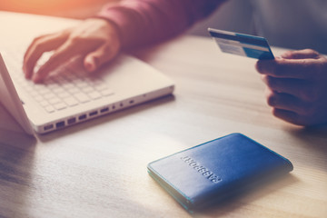 Man holding bank card. Laptop and passport on the table. Web shopping (Intentional sun glare and...