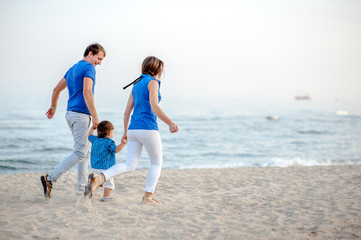 Man woman and child run on the beach near the ocean and feel happy