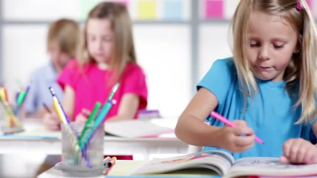 A cute little girl in a classroom setting works diligently on her school task.