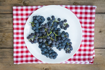 Top view of grapes in white plate on wooden table. fruits top view