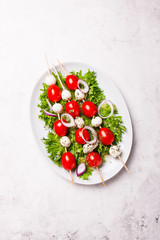 Naklejka na ściany i meble Tomatoes and mozzarella on sticks on salad leaves, top view